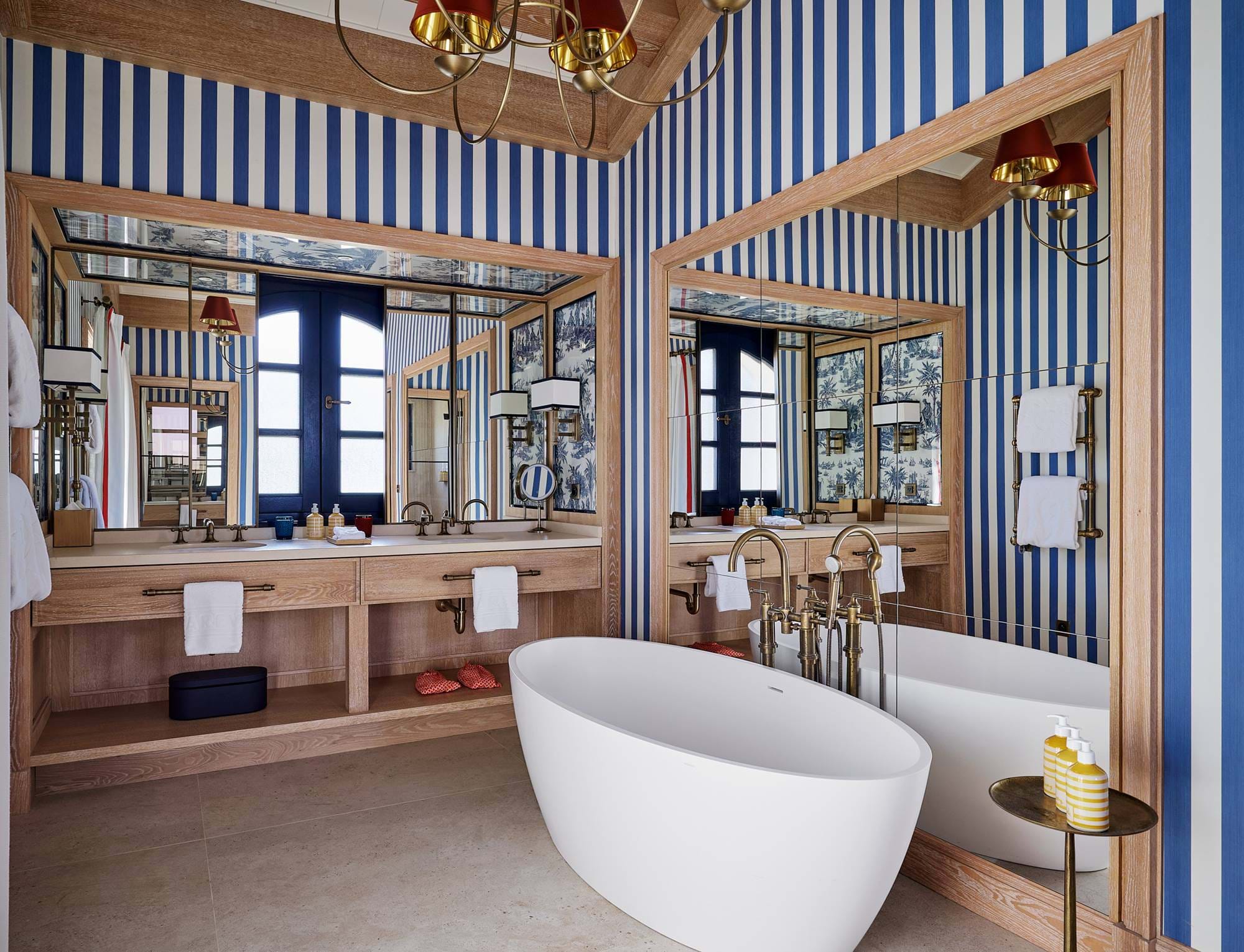 Banheiro elegante no hotel AREV em Saint-Tropez, com banheira branca independente, papel de parede listrado azul e branco e ampla pia dupla de madeira.