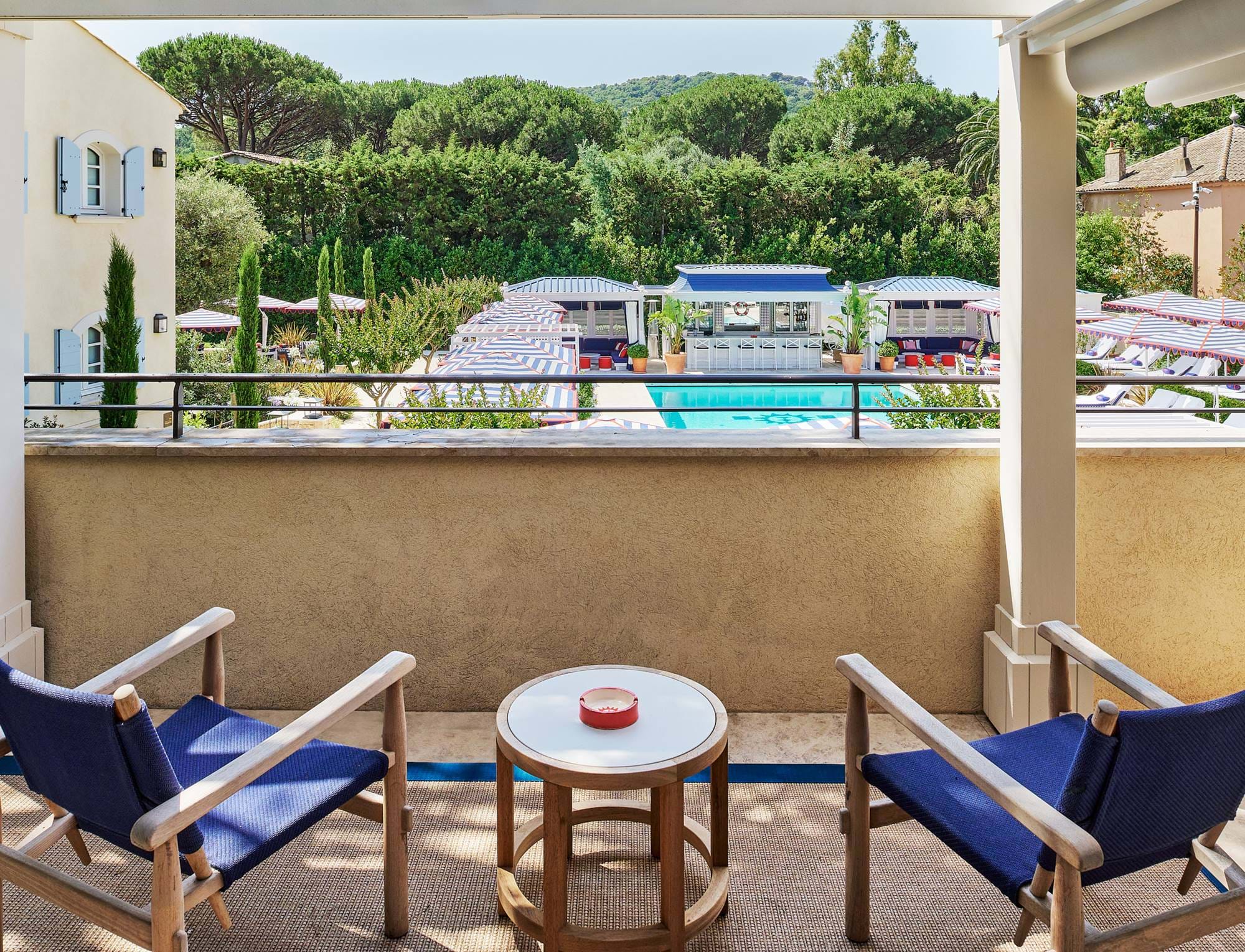 Vista de um terraço privativo no hotel AREV em Saint-Tropez, com espreguiçadeiras azuis, mesa de café e vista para a piscina do hotel rodeada por jardins.