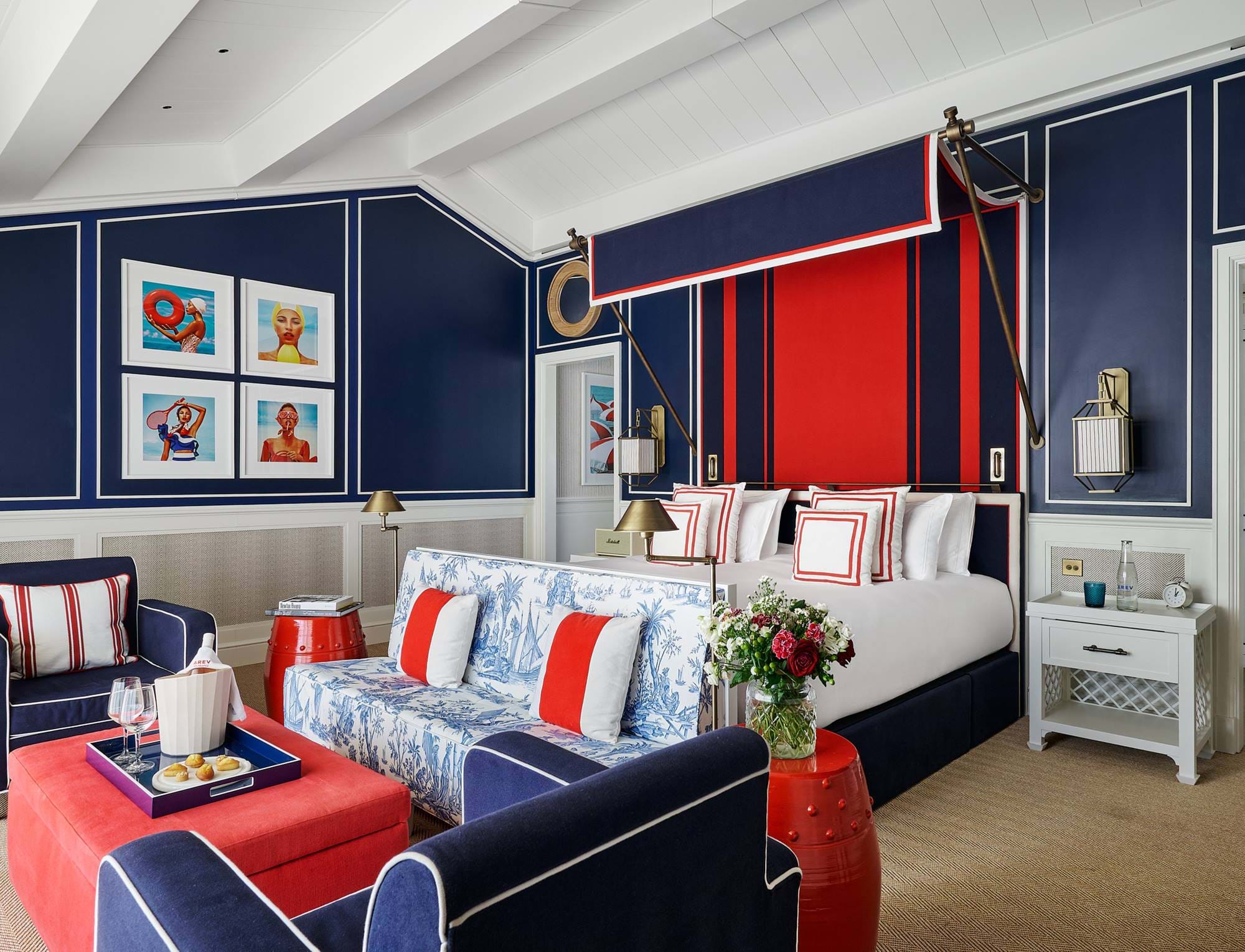 Quarto de luxo com design náutico, apresentando paredes azul-marinho, cama king-size e detalhes em vermelho no hotel AREV em Saint-Tropez.