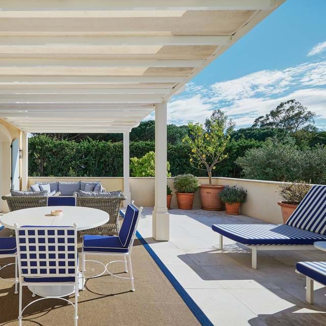 Sonnige Suitenterrasse im AREV Hotel in Saint-Tropez mit blau-weißen Designer-Sonnenliegen und einem Essbereich unter einer Pergola.
