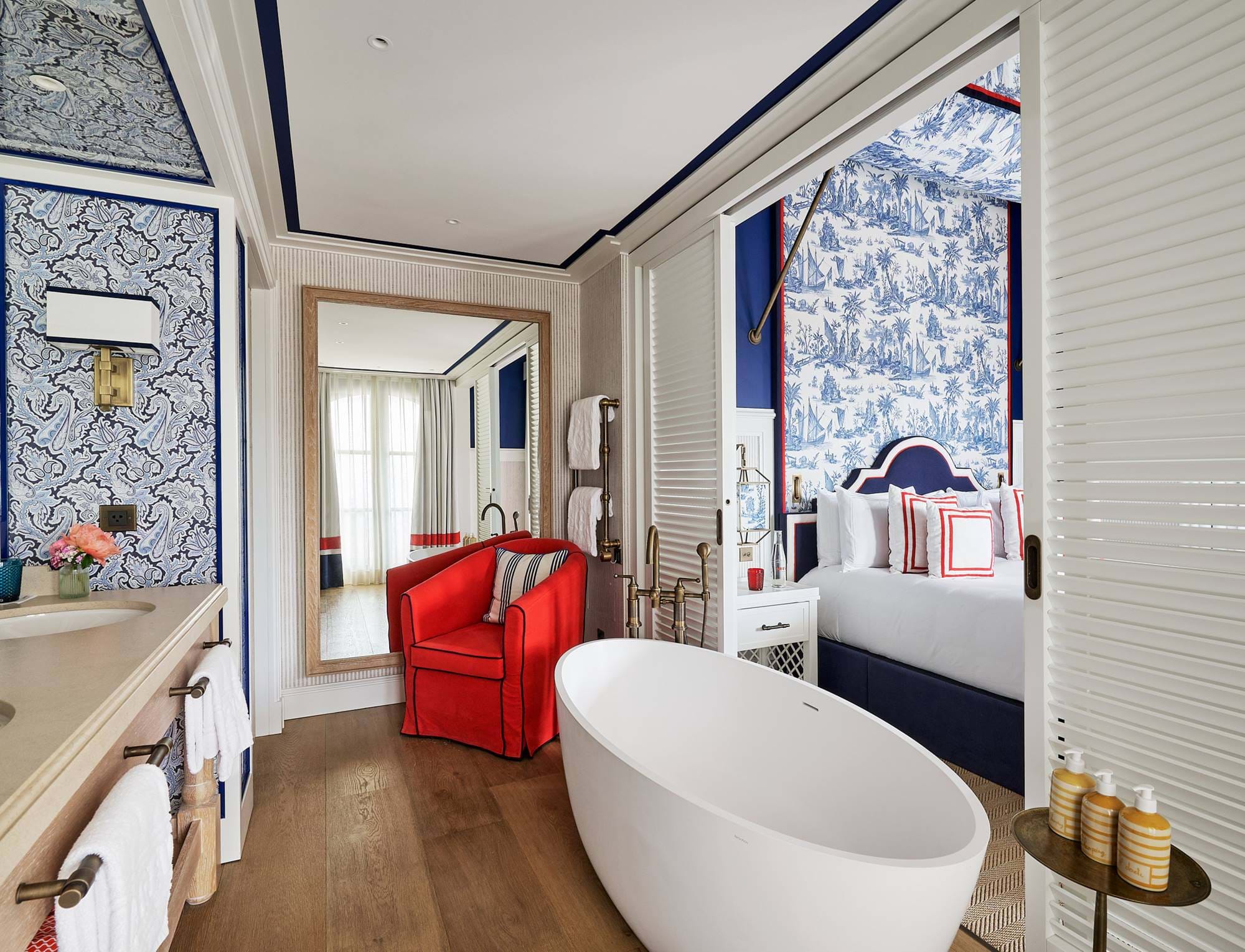 Banheiro luxuoso no hotel AREV em Saint-Tropez, com banheira moderna independente, poltrona vermelha de designer e vista para o quarto elegante.