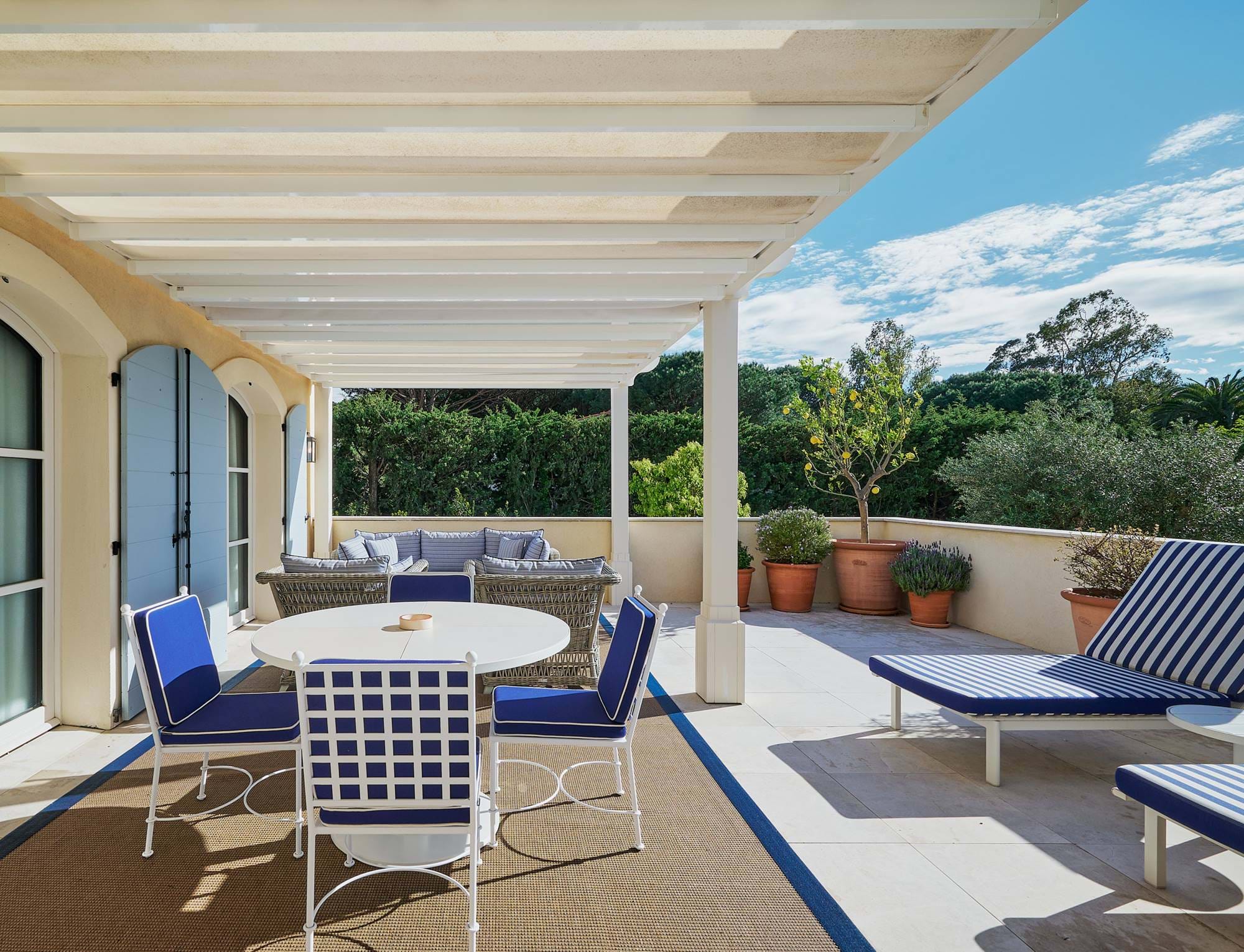 Terraço externo ensolarado com mobiliário azul e branco sob uma pérgola no hotel AREV em Saint-Tropez.