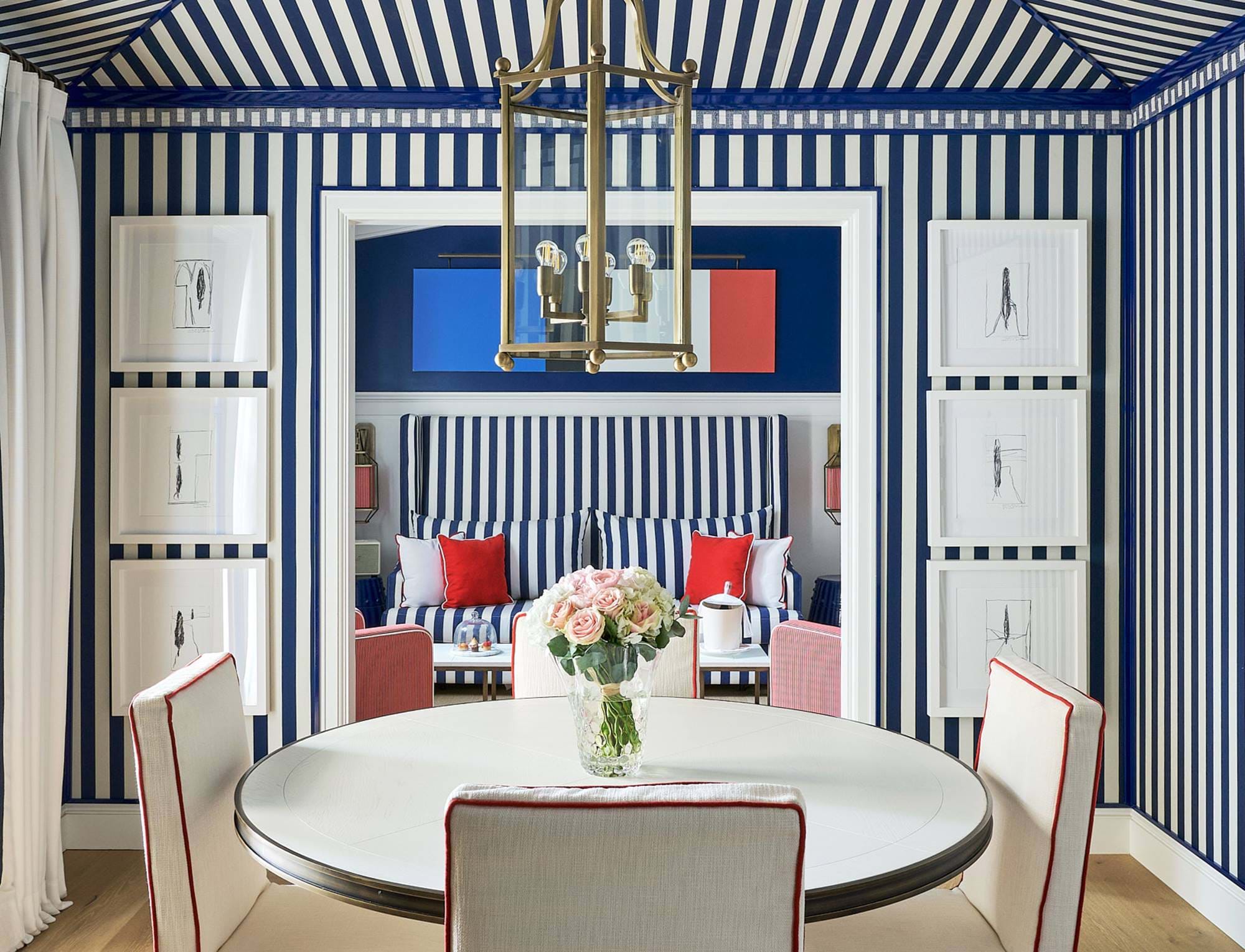 Área de jantar elegante com papel de parede listrado azul e branco no hotel AREV em Saint-Tropez.