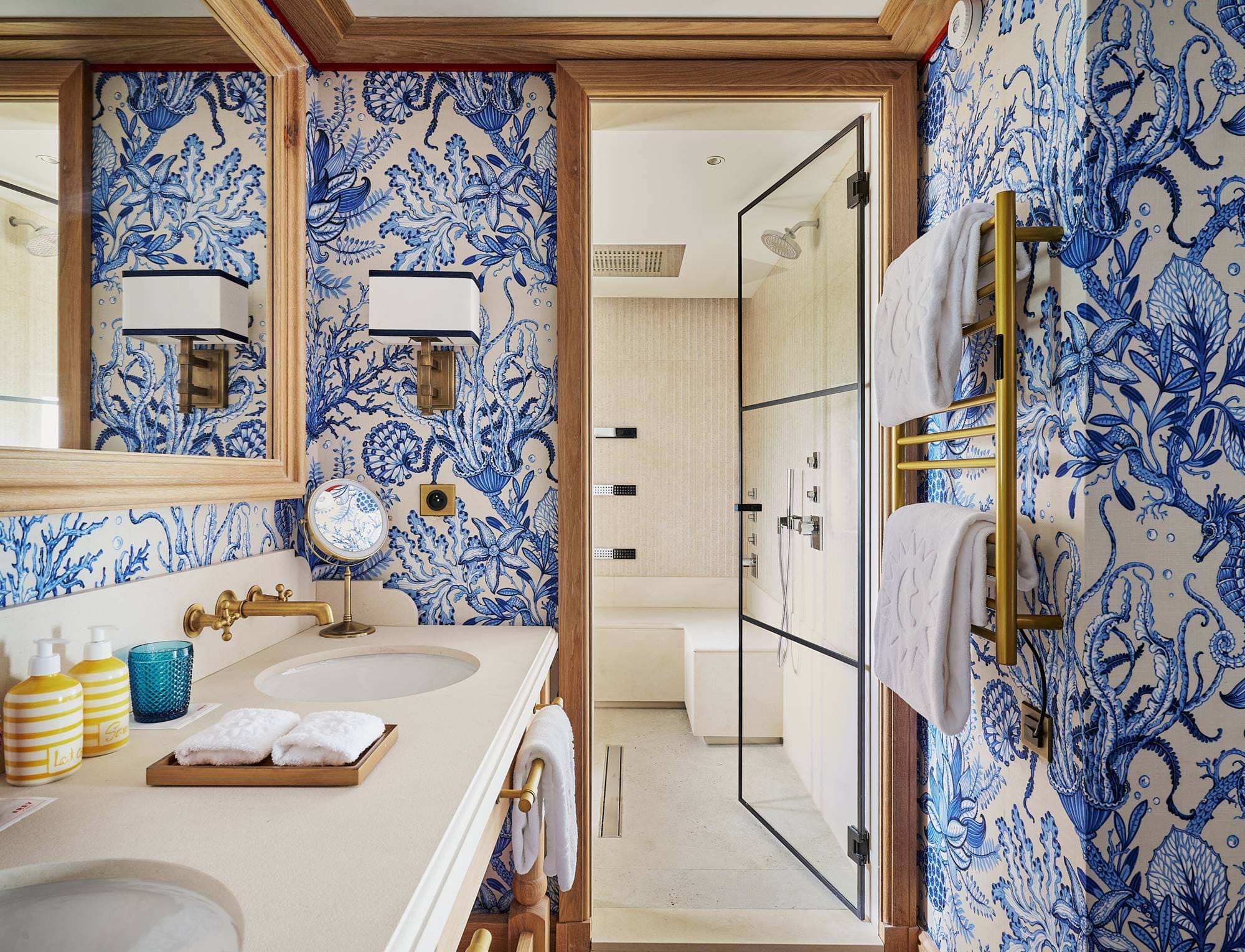 Banheiro luxuoso no hotel AREV em Saint-Tropez, com papel de parede floral azul e branco, pia dupla e moderno chuveiro walk-in.