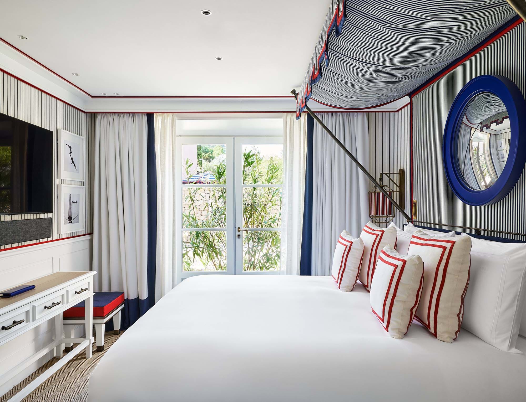 Cama de casal luxuosa com dossel em um quarto iluminado no hotel AREV em Saint-Tropez, decoração elegante em branco e azul com vista para o jardim.