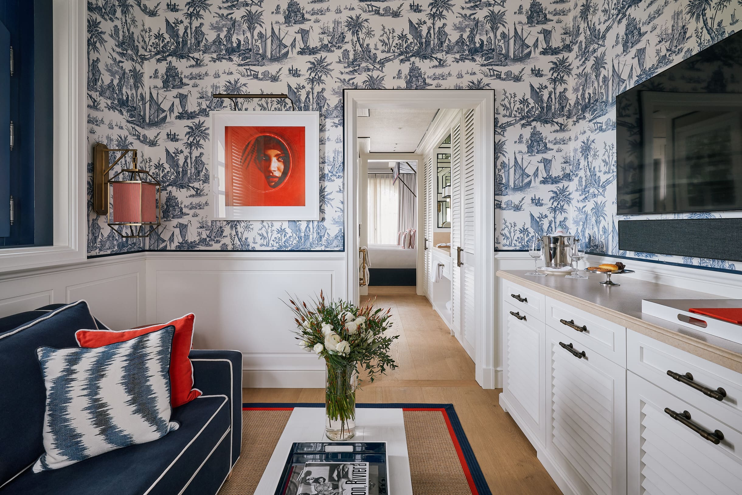 Living room of the One Bedroom Suite at Arev hotel Saint-Tropez, with blue toile de Jouy wallpaper, navy sofa and a red framed artwork