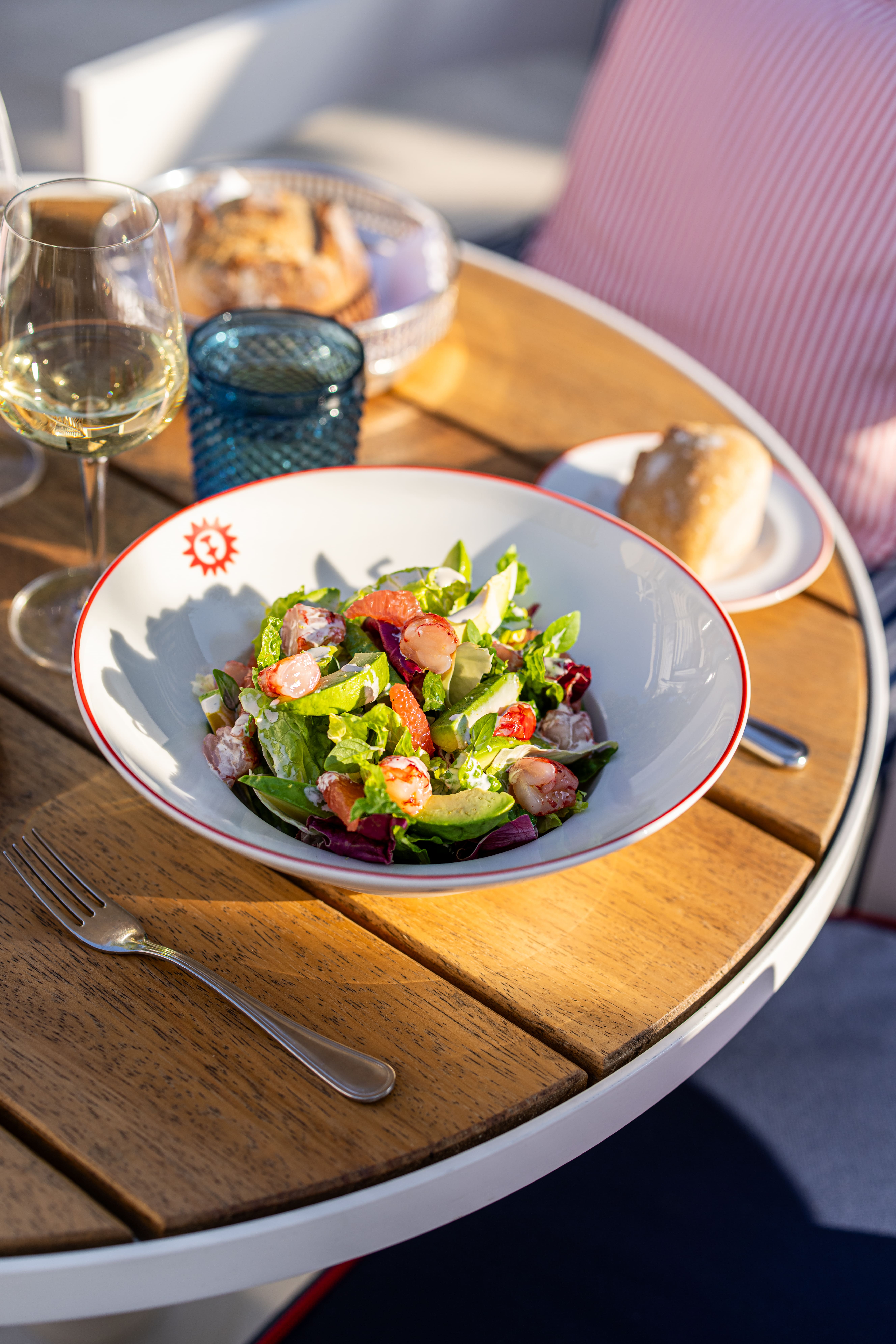 Frischer Salat mit Garnelen, Avocado und Zitrusfrüchten, im Freien im Restaurant des Hotels Arev Saint-Tropez mit einem Glas Weißwein serviert