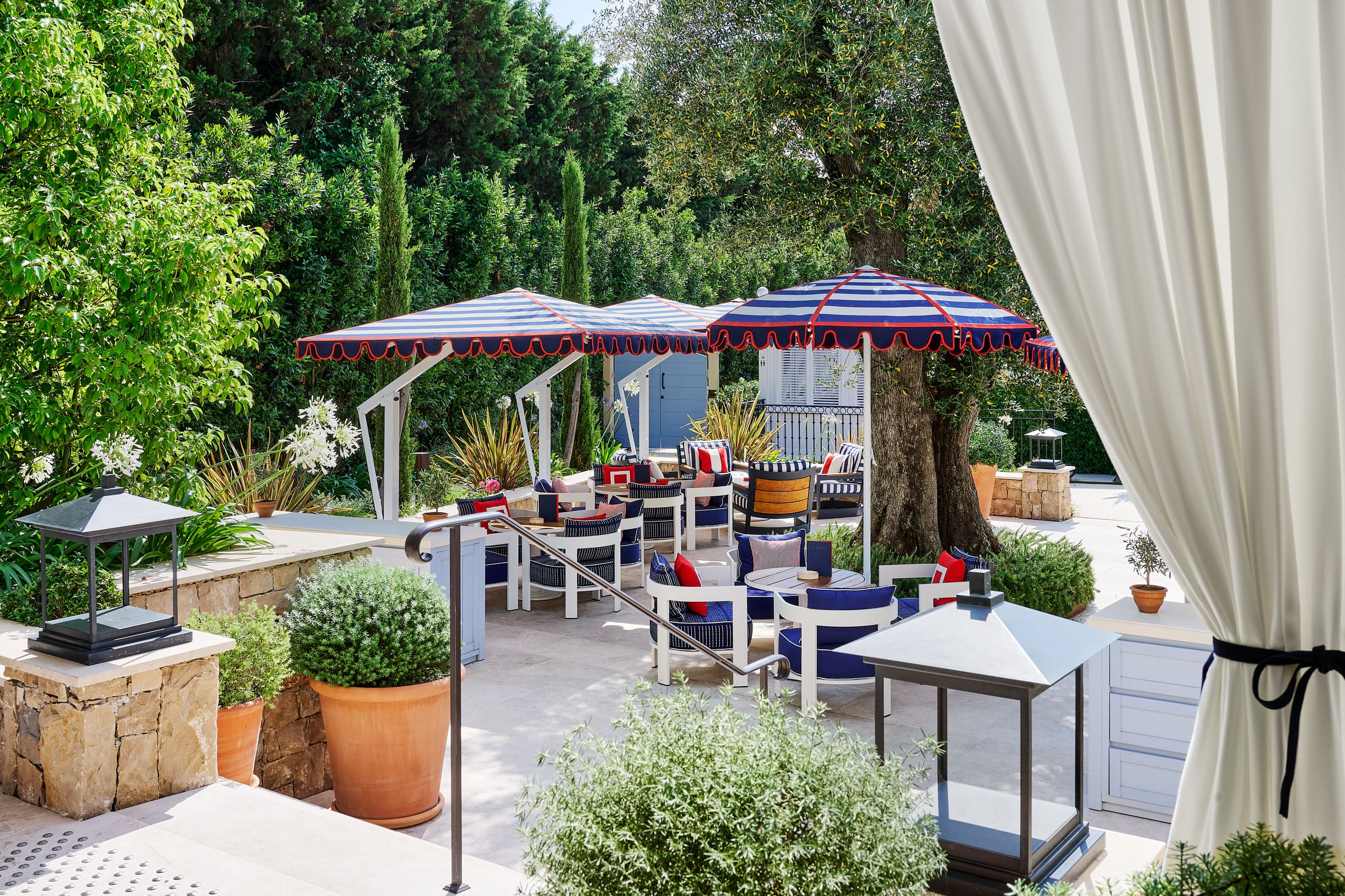 Außenlounge des Hotels Arev in Saint-Tropez mit blau-weiß gestreiften Sonnenschirmen und bunten Sesseln unter Olivenbäumen