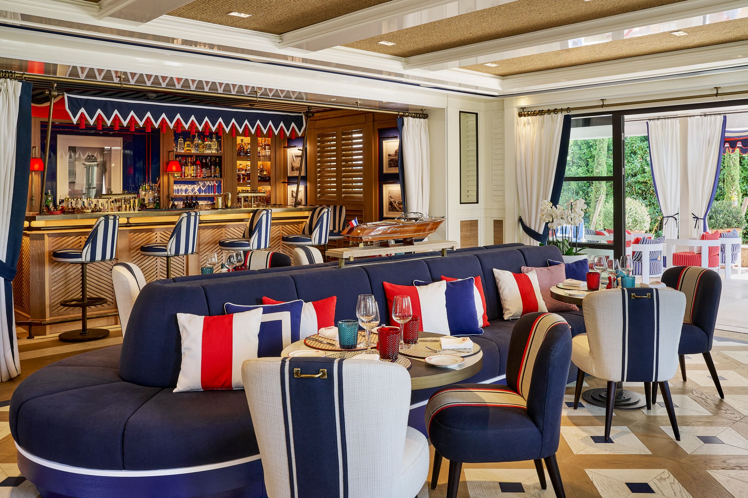 Bar intérieur de l'hôtel Arev à Saint-Tropez, au décor marin bleu-blanc-rouge avec comptoir en bois et coussins colorés