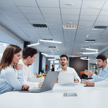 Four young professionals in a modern office engaged in a meeting around a white table with laptops.