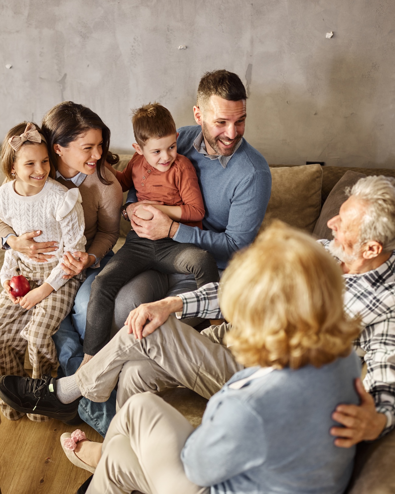 Multigenerational family sitting together at home, grandparents and adult children relaxed and smiling.