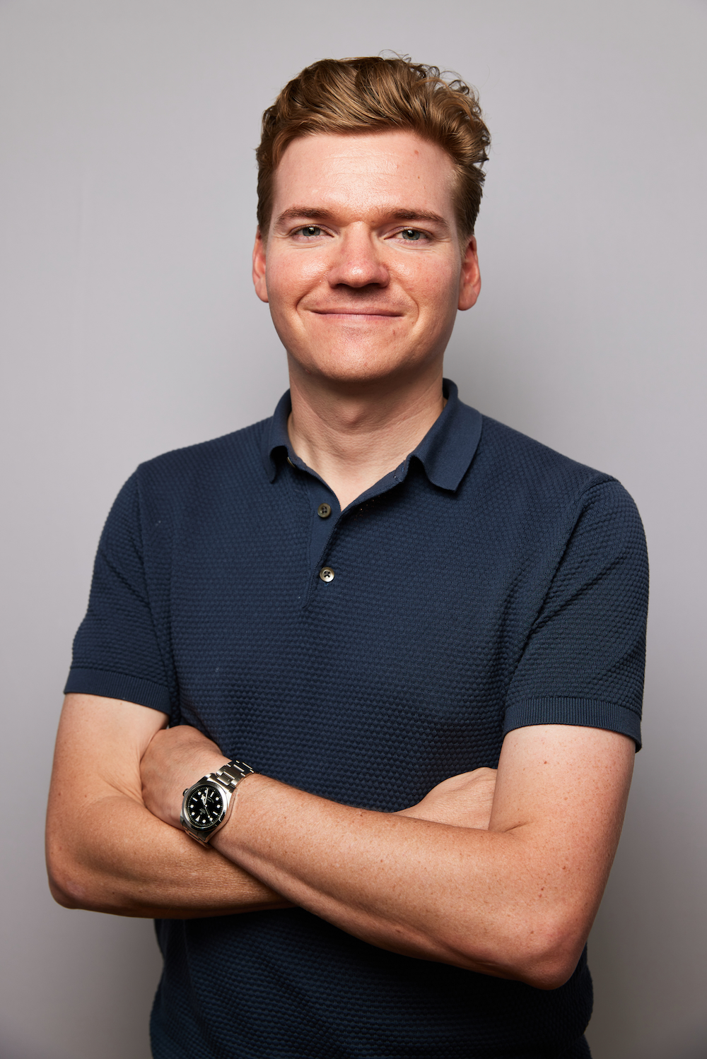 Man with glasses and beard working on a laptop and taking notes on a clipboard in a modern office.