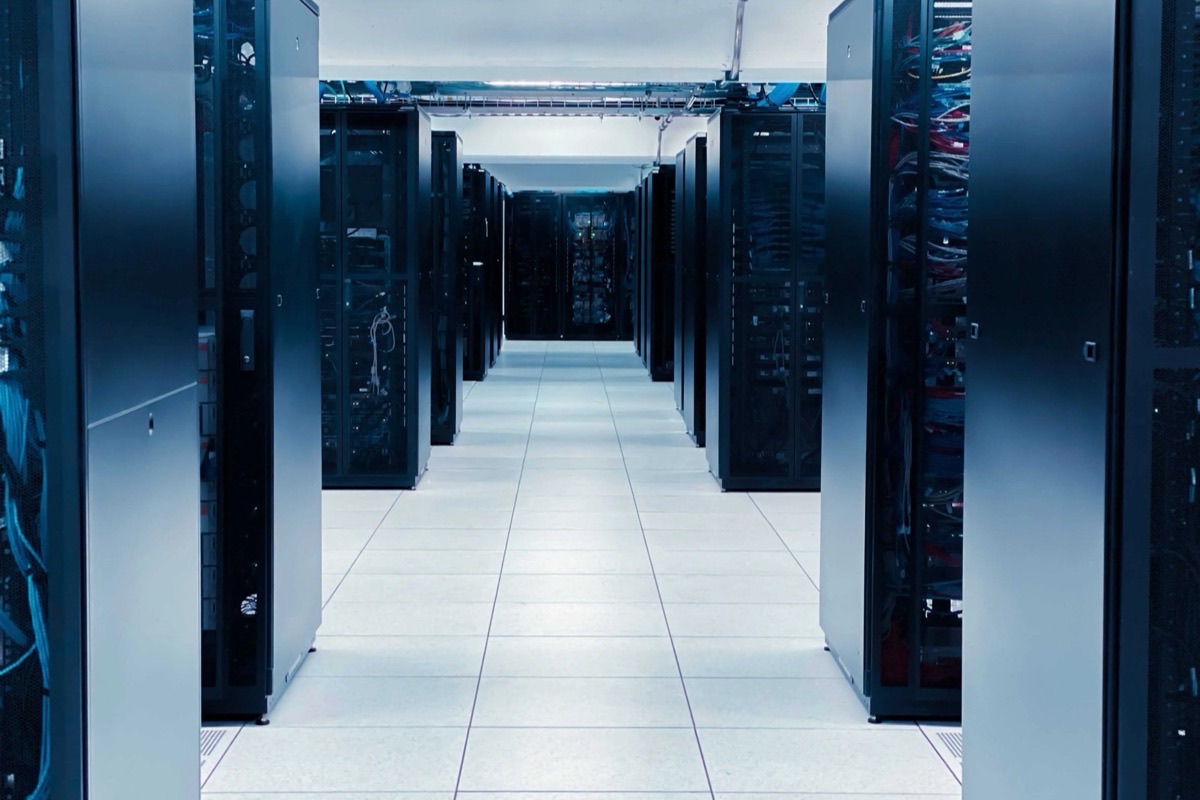 A long, brightly lit aisle between rows of server racks in a data center