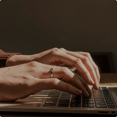 Close-up of hands typing on a laptop keyboard with warm lighting.