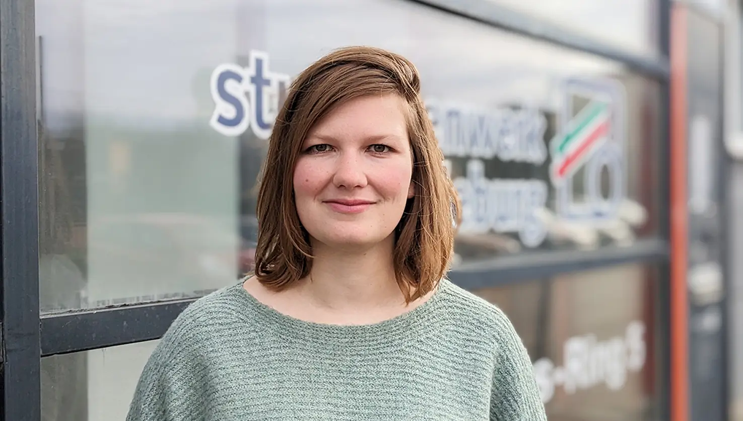Franziska Kaiser steht vor einer Glasfassade mit teilweise sichtbaren Logo des Studentenwerk Magdeburg.