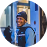 Smiling young man wearing a black beanie and blue backpack standing outdoors in an urban setting.