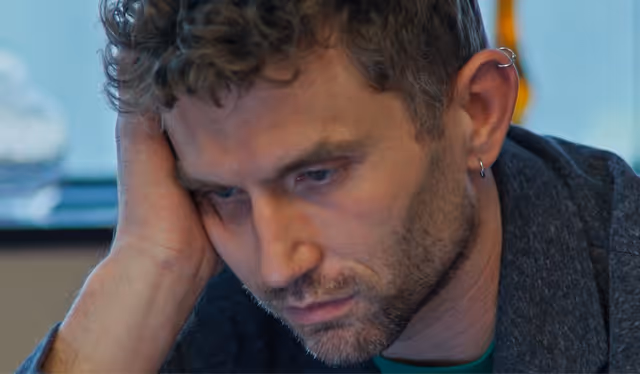 Close-up of a thoughtful man with curly hair resting his head on his hand.