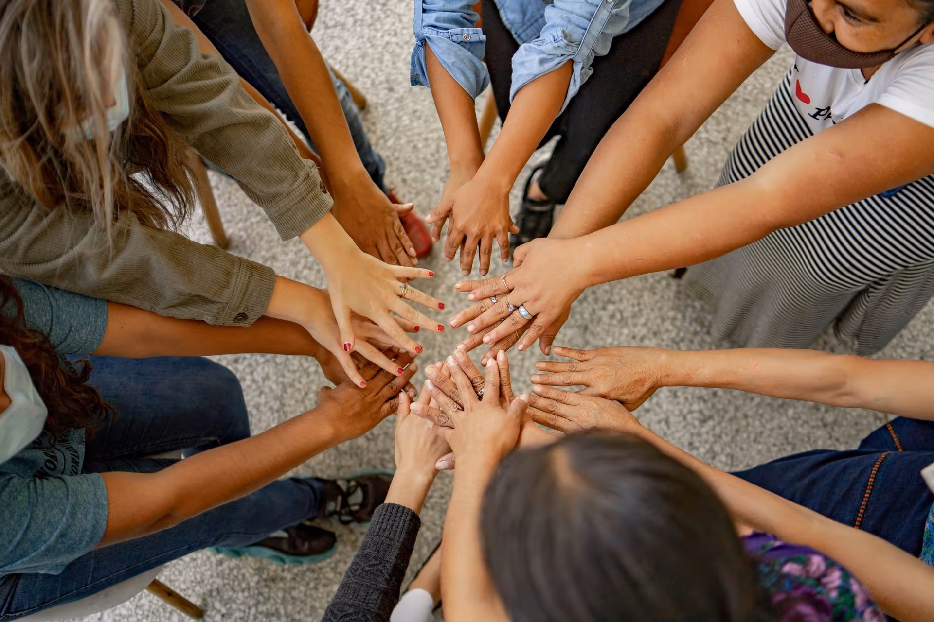 A group of diverse hands reach into the center, symbolizing unity and support. The overall tone is collaborative and inclusive.