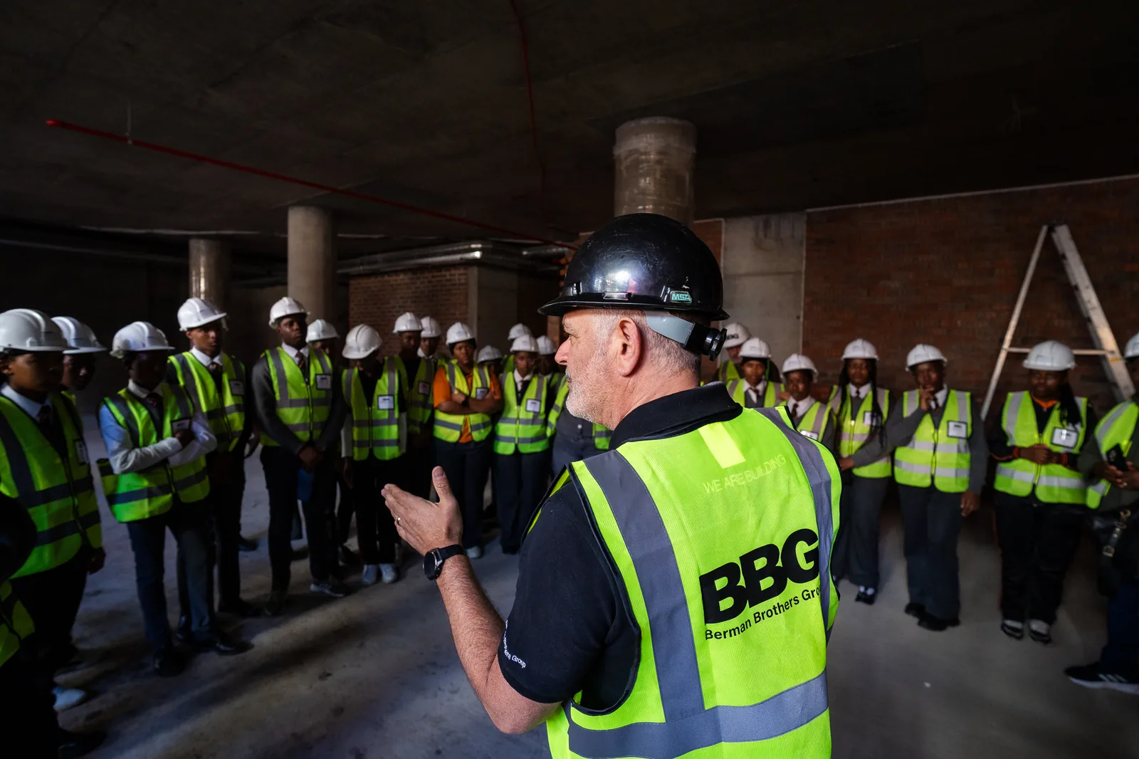 A Berman Brothers Group site manager briefing Hands On learners in hard hats and high-visibility vests inside a building under construction