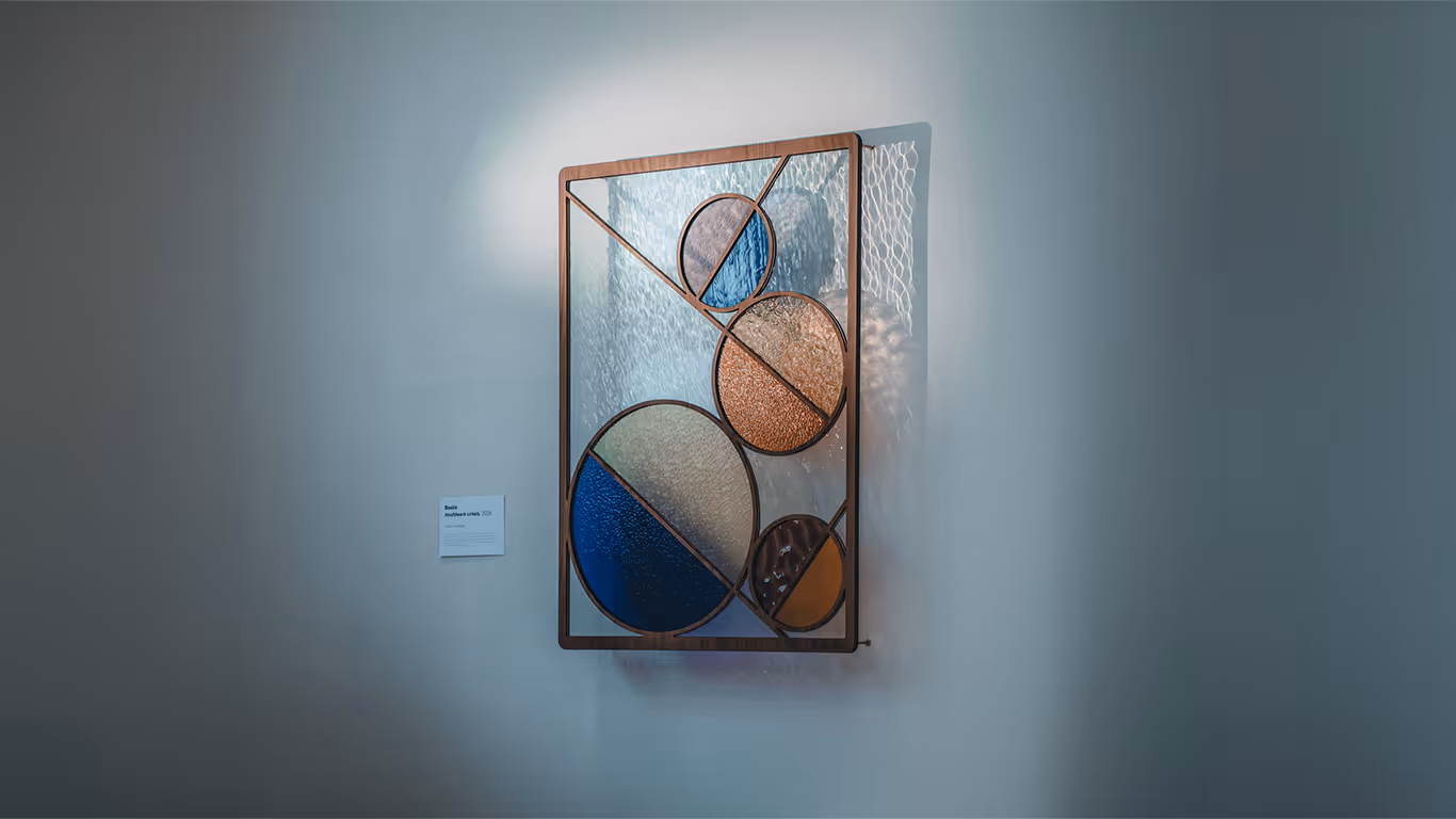 Modern stained glass art featuring textured circles in blue, amber, and clear colors within a rectangular frame mounted on a gray wall.