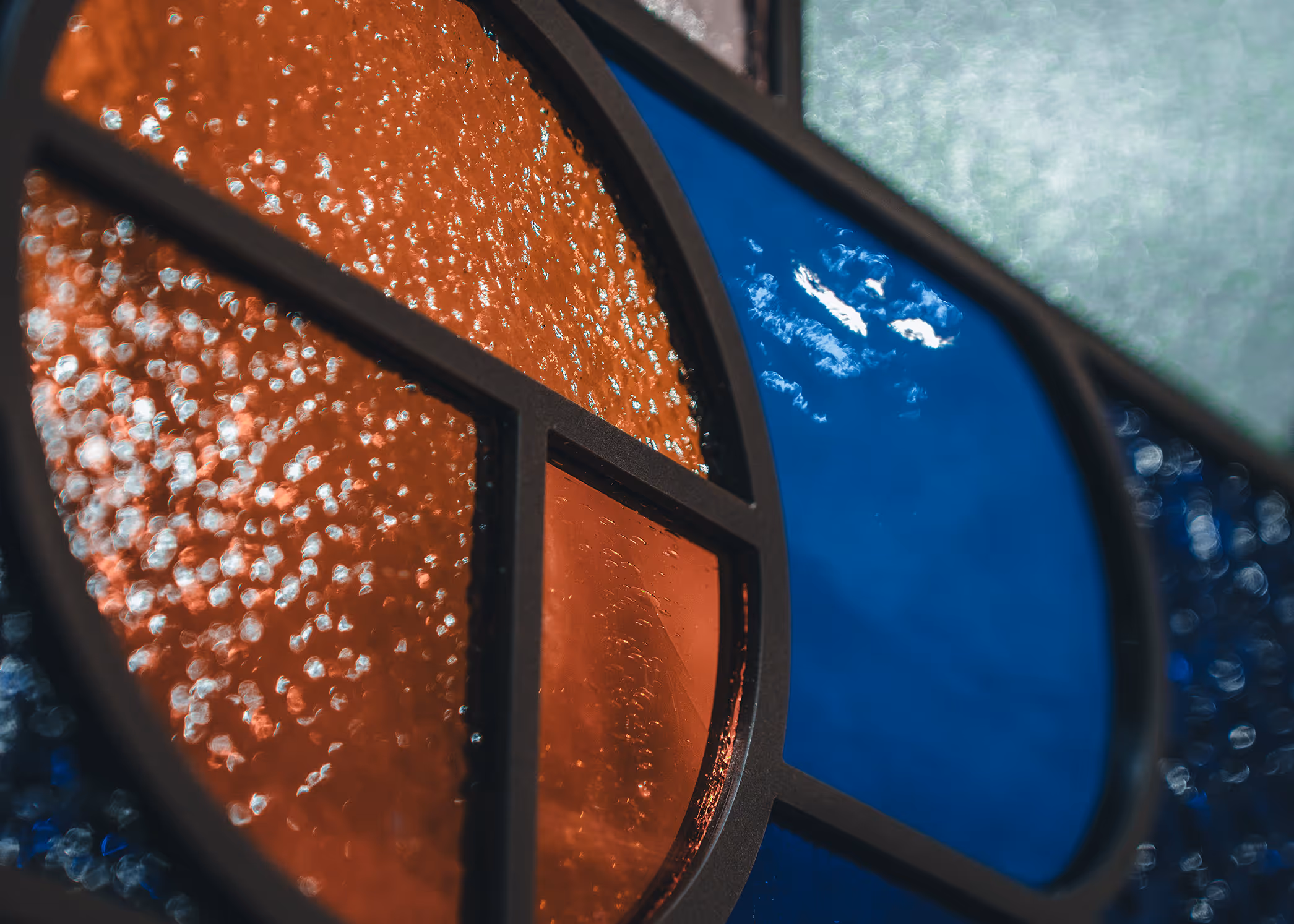 Close-up of textured stained glass panels in orange and blue with black framing.