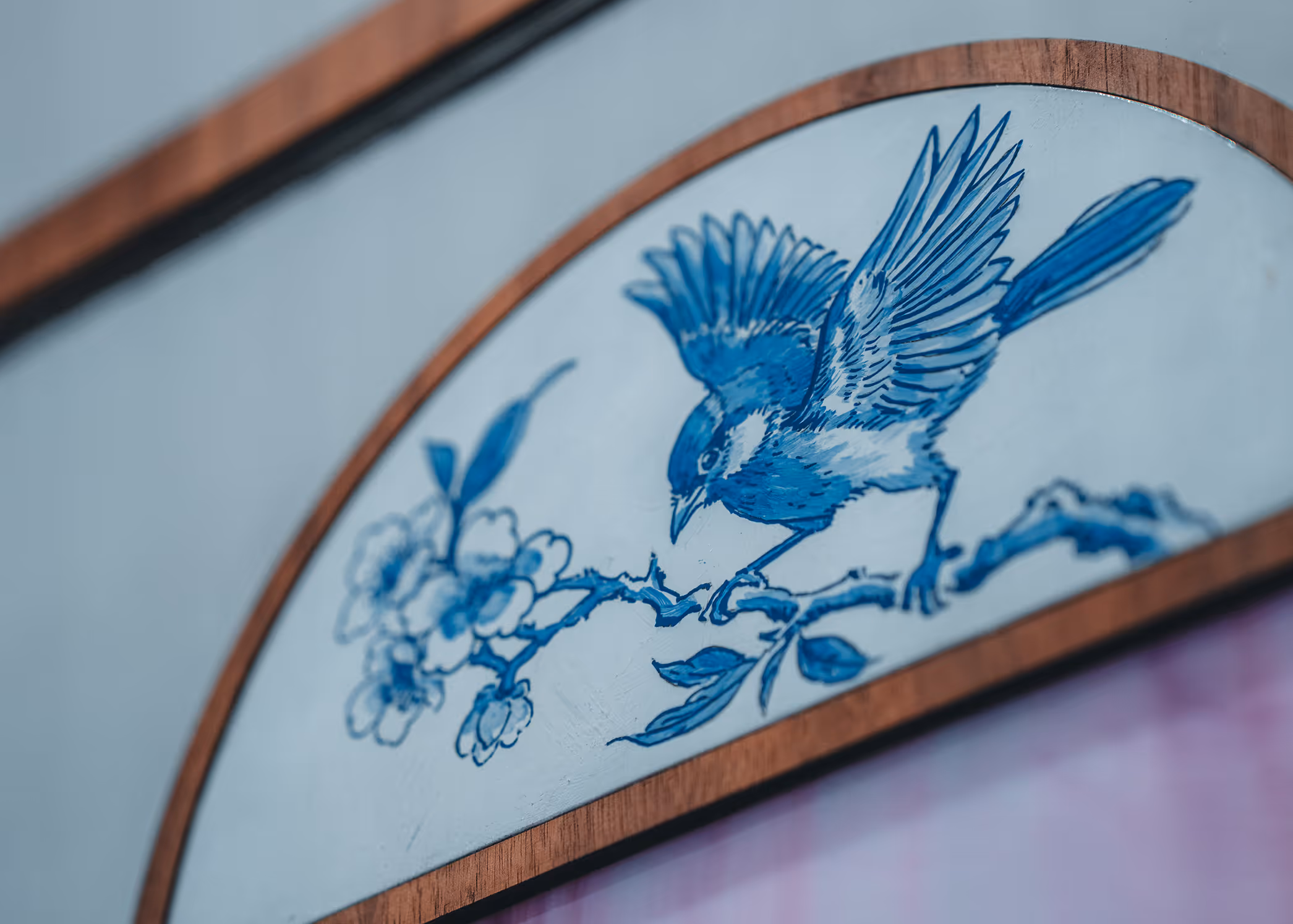 Blue and white painting of a bird with outstretched wings perched on a branch with flowers, framed in wood.