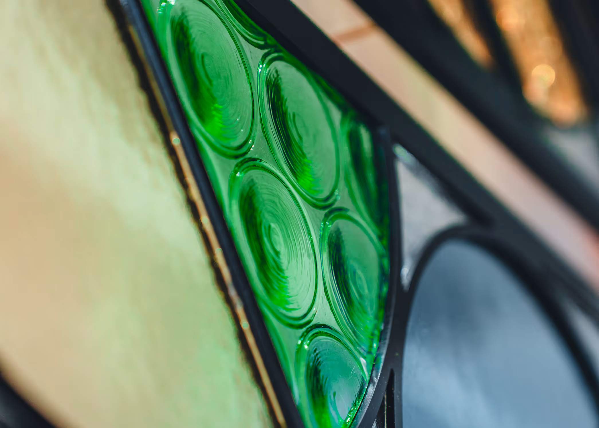 Close-up of a stained glass window with green circular textured glass pieces and surrounding beige and black sections.