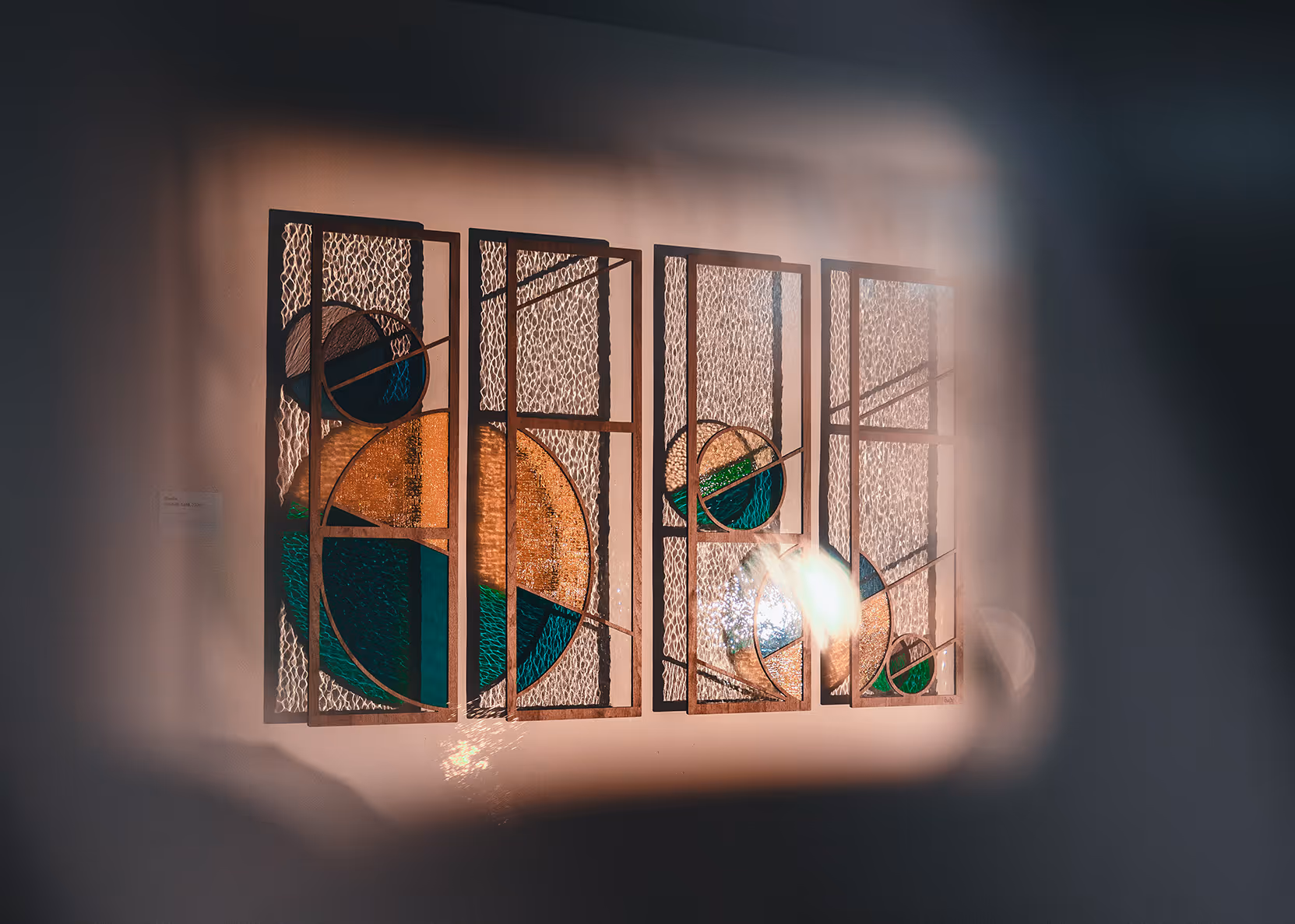 Abstract wall art installation with four rectangular panels featuring geometric circular designs in brown, green, and blue tones against a textured beige background.