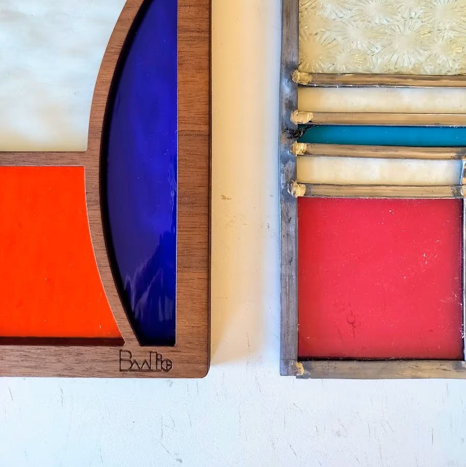 Close-up of two stained glass panels with wooden frames, featuring bold colors including deep blue, red, white, teal, and cream textures.