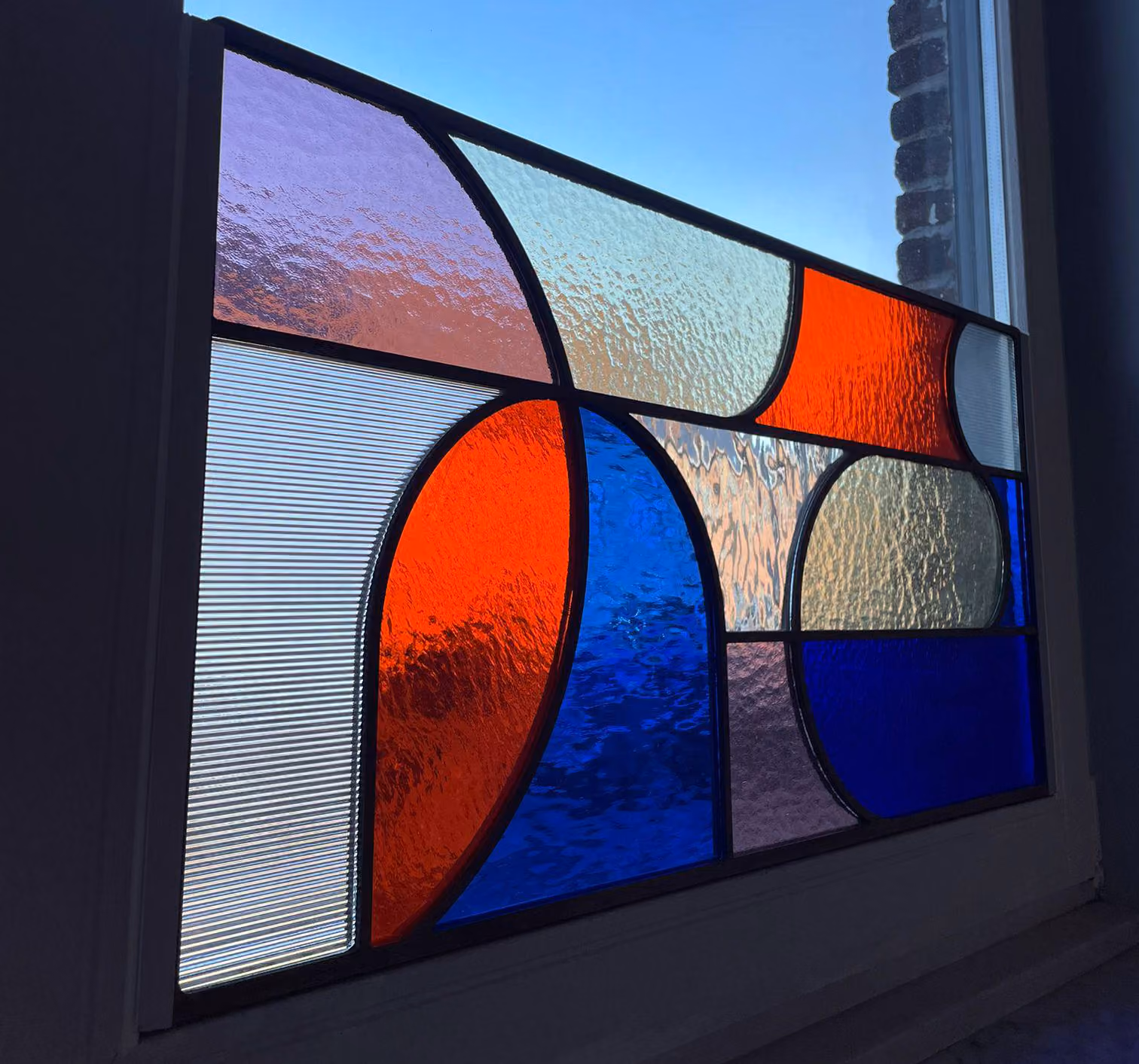Decorative stained glass window with geometric patterns featuring red, blue, purple, and textured clear glass panels.