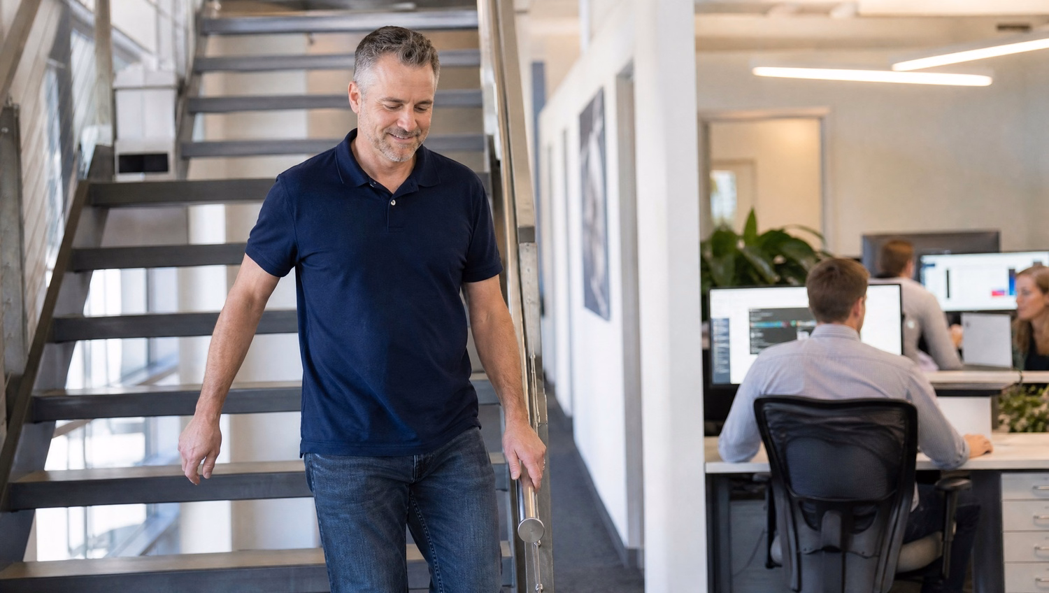 Man in navy polo descending office stairs, hand on railing 70