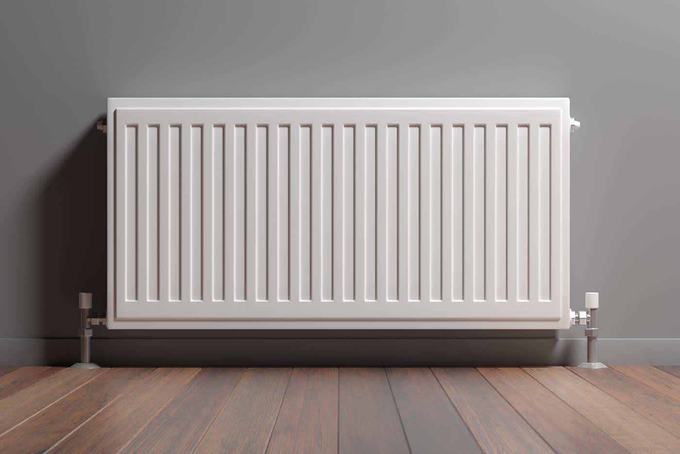 White wall-mounted radiator installed on a gray wall above wooden floorboards.