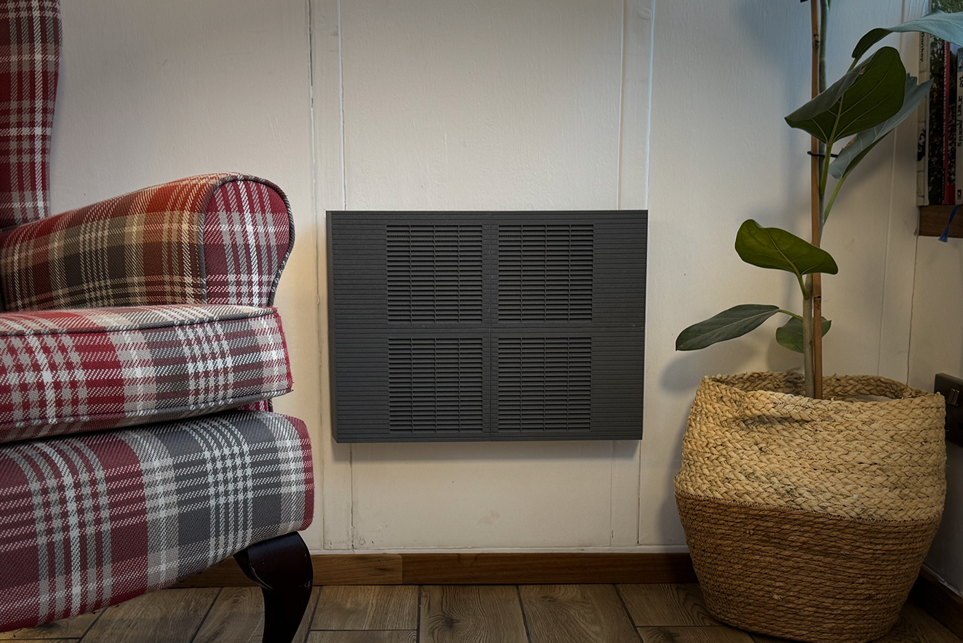 Black wall-mounted Trimley between a red plaid armchair and a woven basket with a green plant.