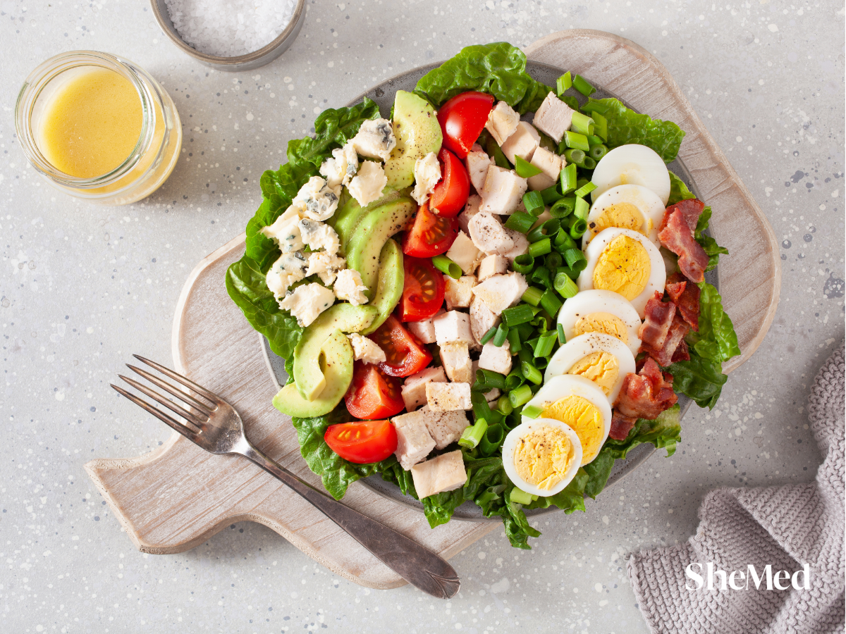A vibrant bowl of mixed salad featuring fresh greens, cherry tomatoes, cucumbers, and sliced carrots, eggs, topped with a light dressing