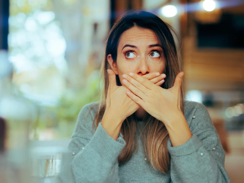 Woman covering her mouth with both hands looking uncomfortable, representing nausea as a medication side effect.