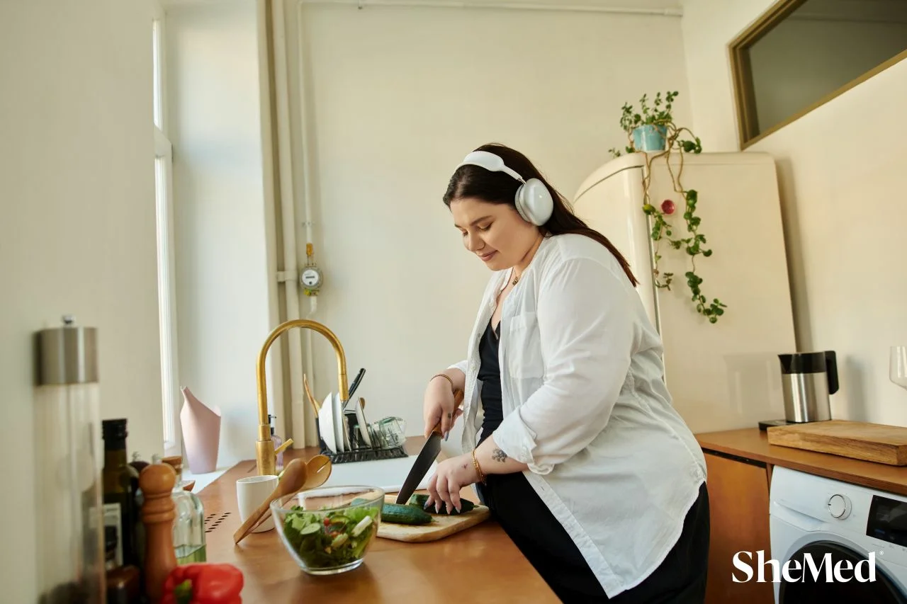 Woman wearing headphones chopping fresh vegetables on a wooden board while preparing a healthy meal at home.