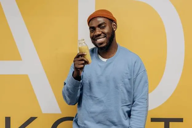Happy man in blue sweater holding a nutritious drink against a yellow background.