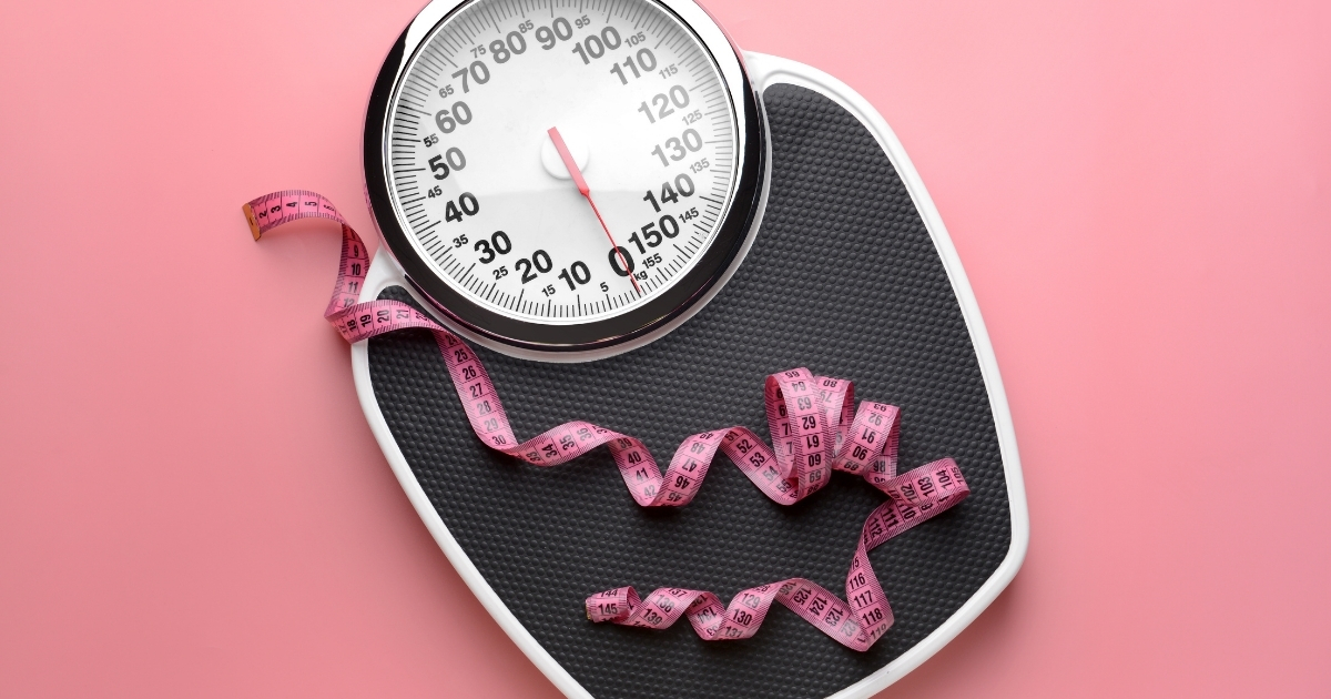 Bathroom scales with a pink measuring tape on a pink background
