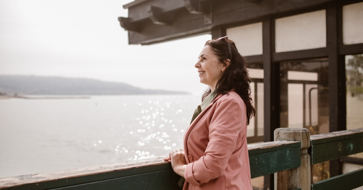 Woman in a pink blazer smiling and looking out of a window