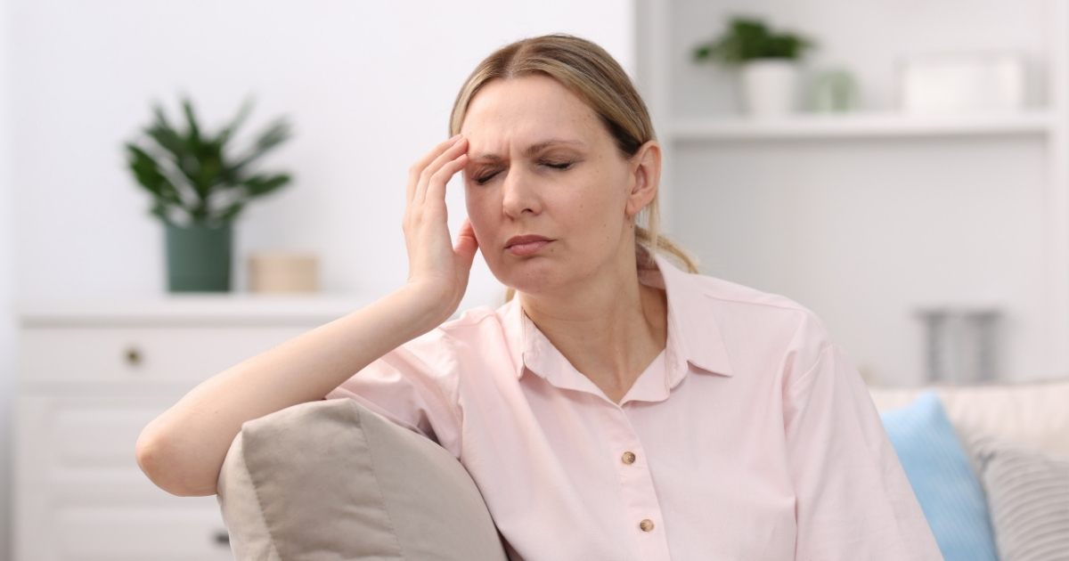 Woman sitting on a couch in pink clothing holding her head in discomfort