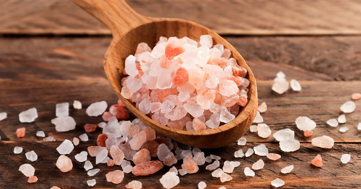 Wooden spoon and scattered pink Himalayan salt crystals on a wooden surface
