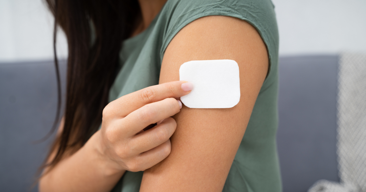 Close-up of a person applying a white adhesive patch to their upper arm