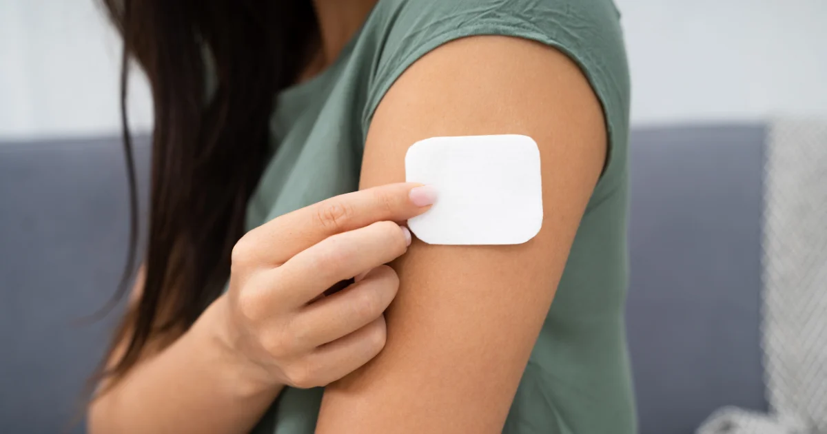 Close-up of a person applying a white adhesive patch to their upper arm