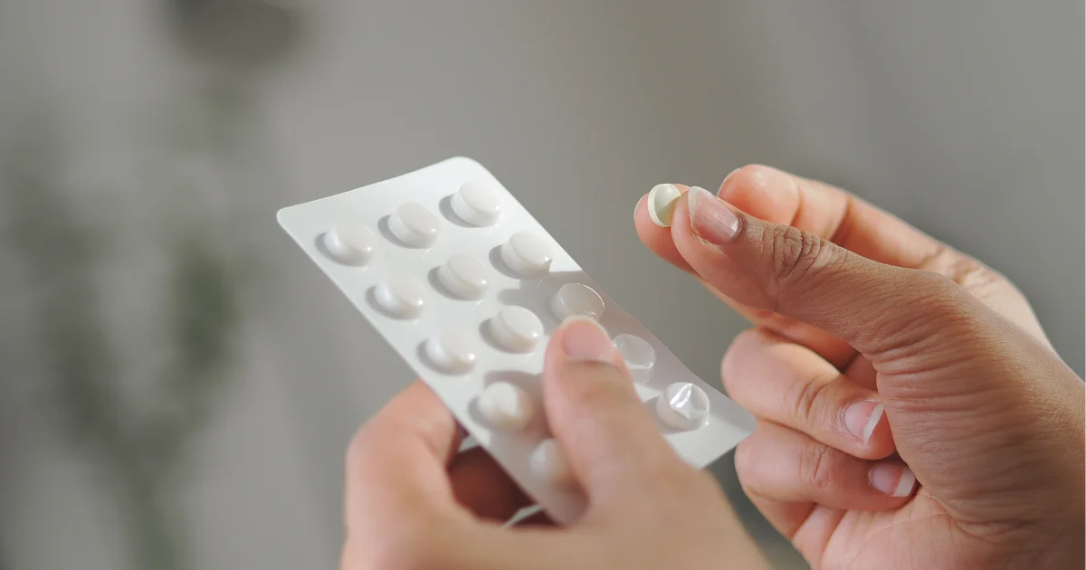 Close-up of a hand holding a single tablet above a blister pack of pills, illustrating orforglipron dosing