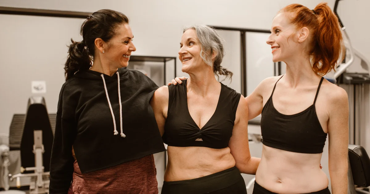 Three smiling women in gym wear standing together in a fitness studio