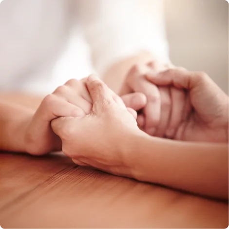 Two people holding hands gently over a wooden table, symbolizing support and connection.