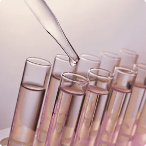 Close-up of a dropper releasing a liquid drop into one of several glass test tubes filled with clear liquid.