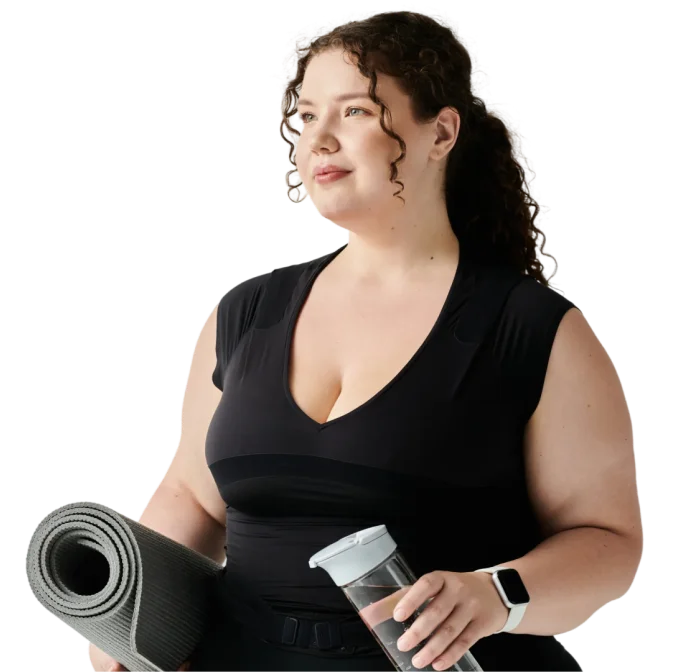 Woman with curly hair in black workout clothes holding a rolled yoga mat and a clear water bottle.