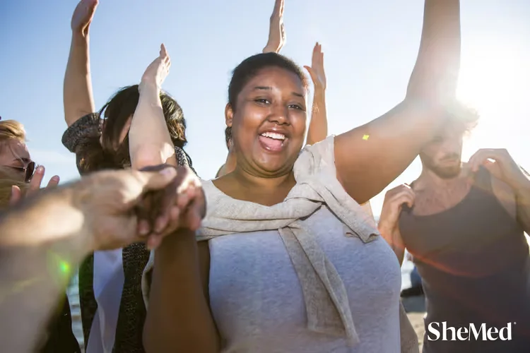 Group of diverse young adults dancing and celebrating outdoors in sunlight.