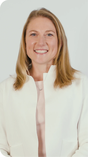 Smiling woman with shoulder-length blonde hair wearing a white blazer and light pink top against a plain light background.